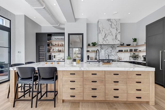 kitchen with light wood-type flooring, light brown cabinetry, a breakfast bar, and light stone counters