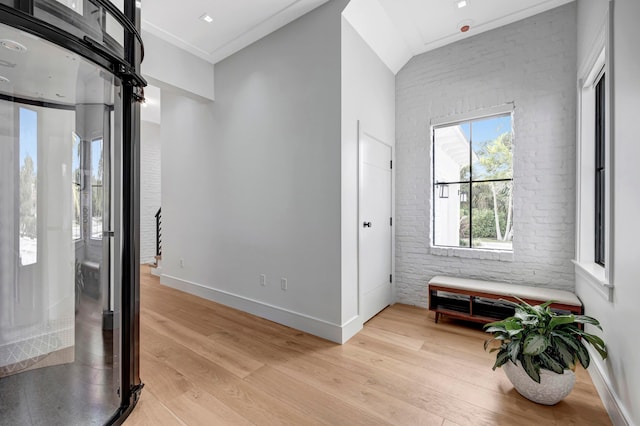 foyer featuring brick wall, light hardwood / wood-style floors, and crown molding