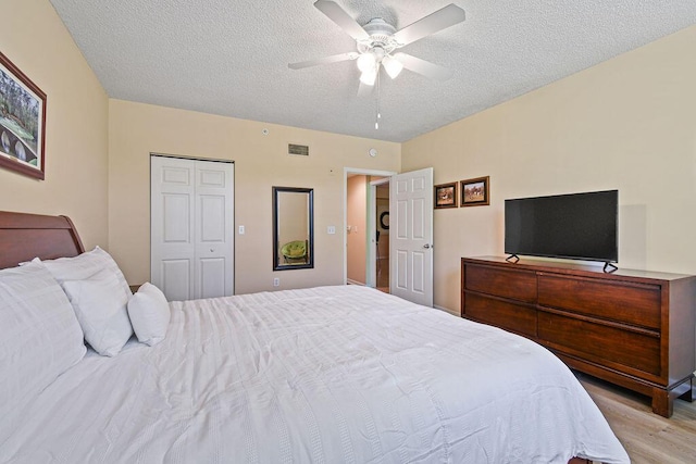 bedroom with ceiling fan, a closet, light hardwood / wood-style flooring, and a textured ceiling