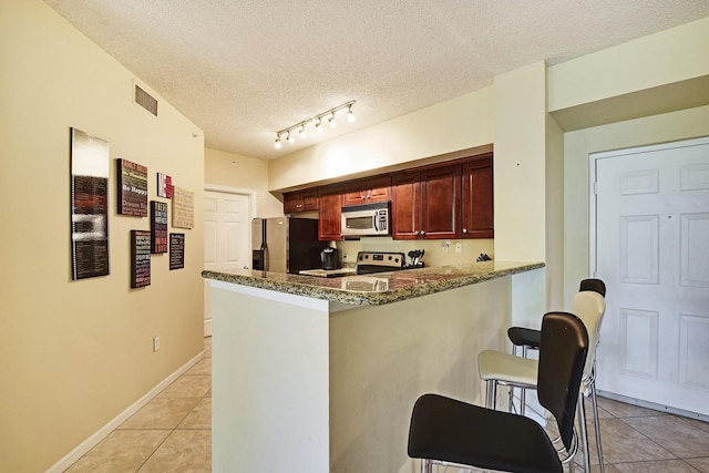 kitchen with stainless steel appliances, dark stone counters, a textured ceiling, a breakfast bar, and track lighting