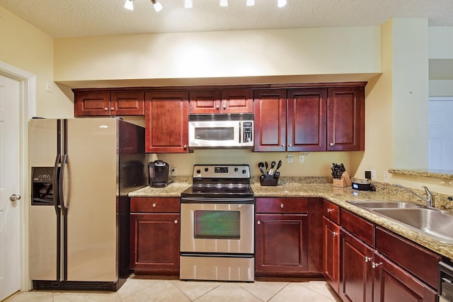 kitchen with sink, light tile floors, stainless steel appliances, light stone countertops, and a textured ceiling