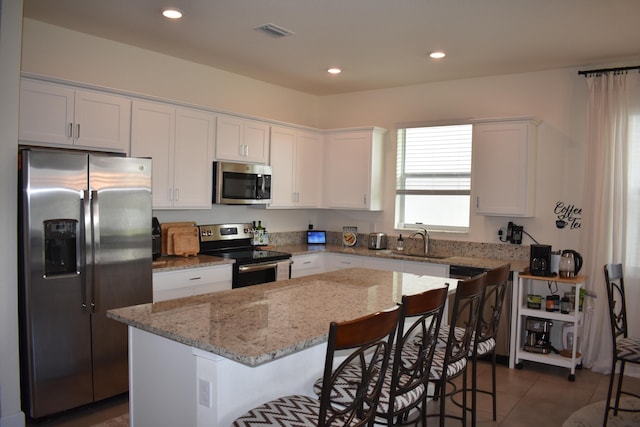 kitchen featuring sink, white cabinets, appliances with stainless steel finishes, light stone countertops, and a center island