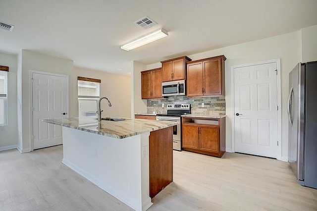 kitchen featuring light stone countertops, sink, an island with sink, stainless steel appliances, and tasteful backsplash