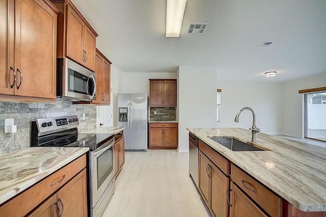 kitchen featuring backsplash, light hardwood / wood-style floors, sink, stainless steel appliances, and light stone counters