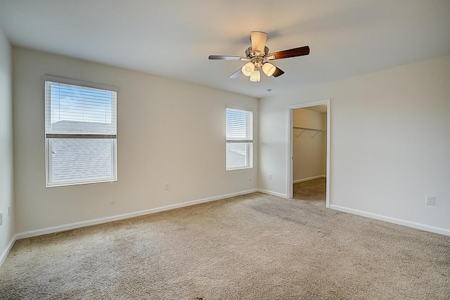 unfurnished bedroom with light carpet, a walk in closet, a closet, and ceiling fan