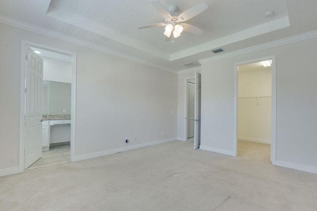 unfurnished bedroom with a spacious closet, a raised ceiling, ensuite bath, and light colored carpet