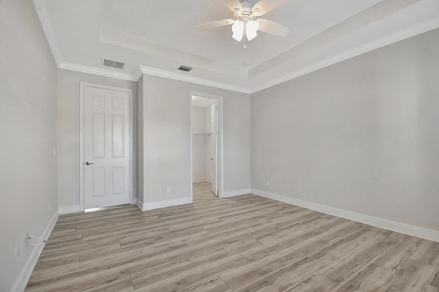 unfurnished bedroom featuring a closet, a walk in closet, ceiling fan, light hardwood / wood-style flooring, and a raised ceiling