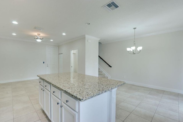 kitchen with light stone countertops, light tile floors, white cabinets, a center island, and crown molding