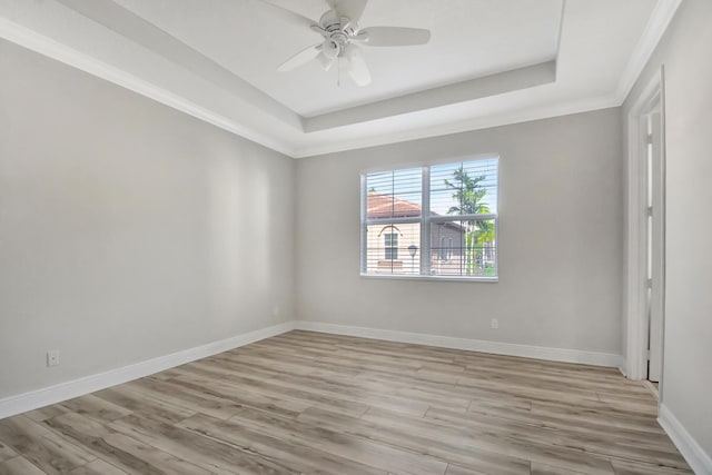 empty room with a raised ceiling, crown molding, ceiling fan, and light hardwood / wood-style flooring