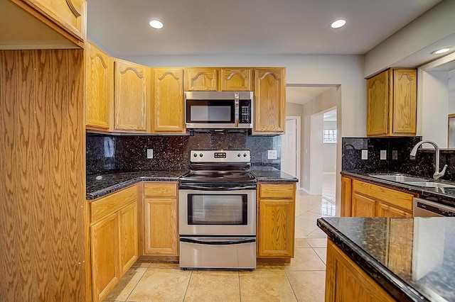 kitchen with sink, stainless steel appliances, light tile floors, dark stone counters, and tasteful backsplash