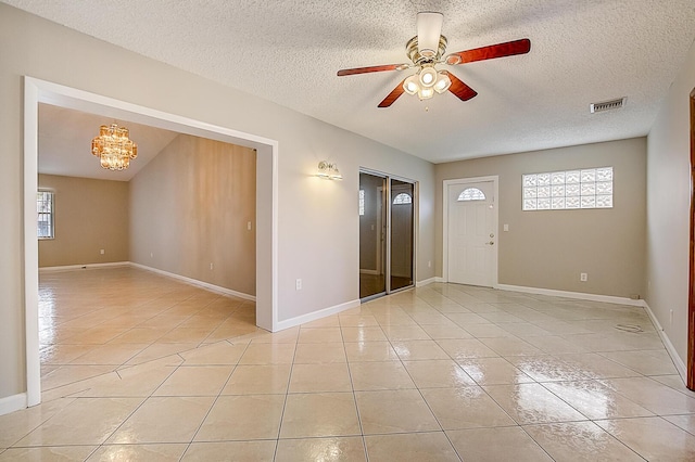 tiled spare room featuring a textured ceiling, ceiling fan with notable chandelier, and a wealth of natural light