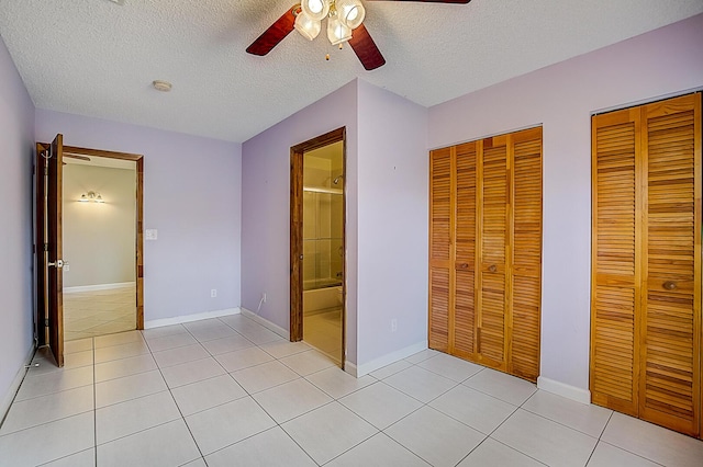 unfurnished bedroom featuring light tile flooring, two closets, ceiling fan, and a textured ceiling