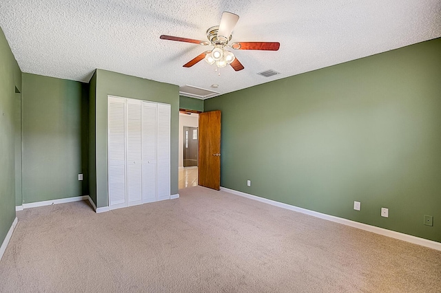 unfurnished bedroom with light carpet, a closet, ceiling fan, and a textured ceiling