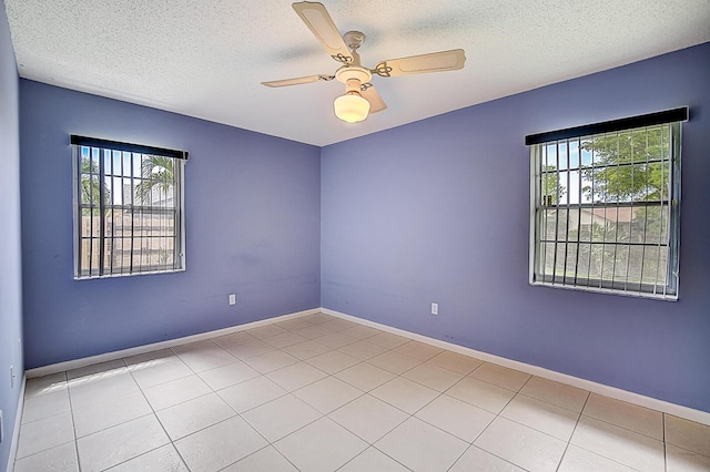 empty room featuring a textured ceiling, ceiling fan, light tile floors, and a wealth of natural light