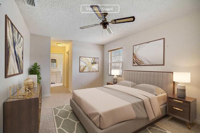 bedroom with connected bathroom, a textured ceiling, light colored carpet, and ceiling fan