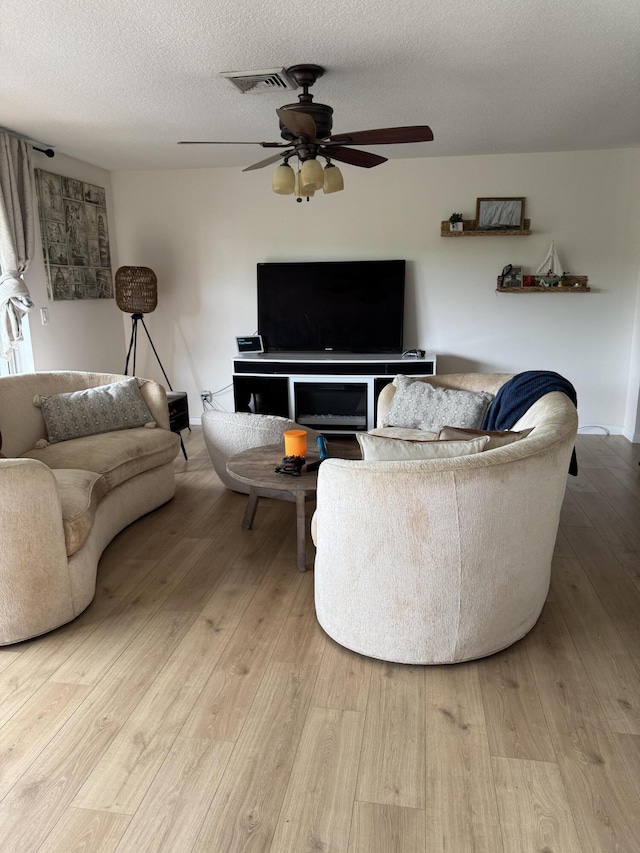 living area with a ceiling fan, wood finished floors, and a textured ceiling