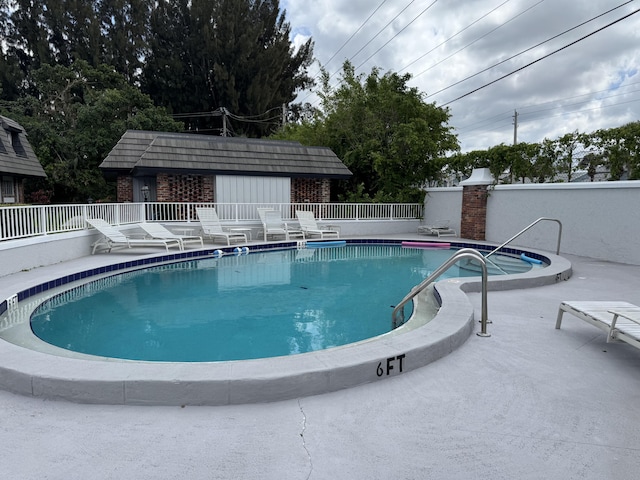 community pool featuring fence, an outbuilding, and a patio area
