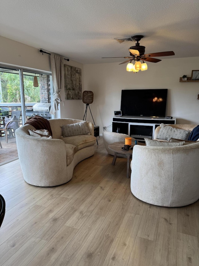 living room featuring light wood finished floors, ceiling fan, and a textured ceiling