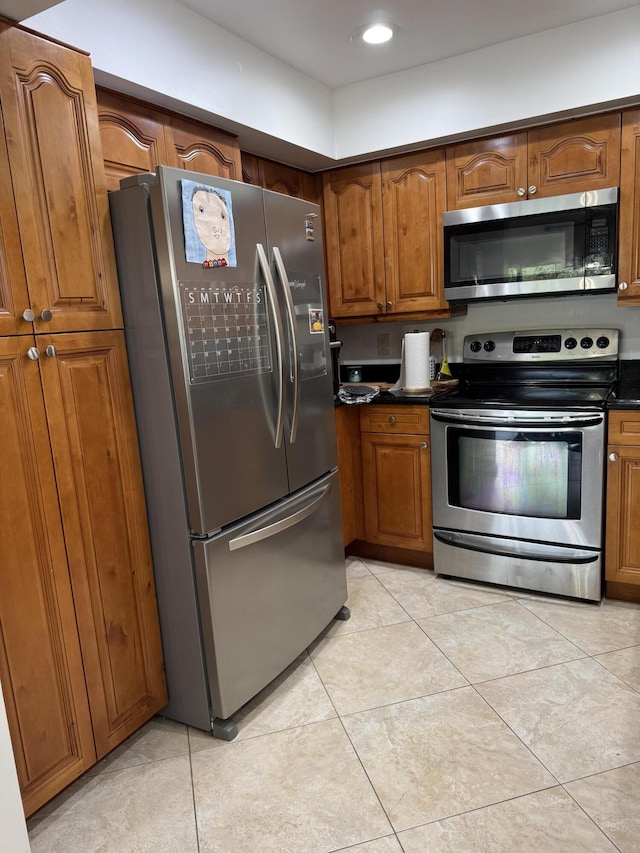 kitchen featuring appliances with stainless steel finishes, brown cabinets, dark countertops, light tile patterned floors, and recessed lighting