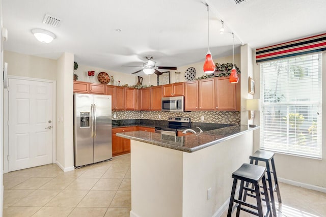 kitchen featuring decorative light fixtures, ceiling fan, kitchen peninsula, appliances with stainless steel finishes, and backsplash