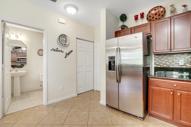 kitchen featuring sink, light tile floors, dark stone counters, stainless steel appliances, and tasteful backsplash