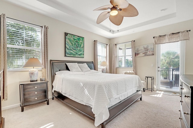 bedroom with a raised ceiling, multiple windows, ceiling fan, and light colored carpet