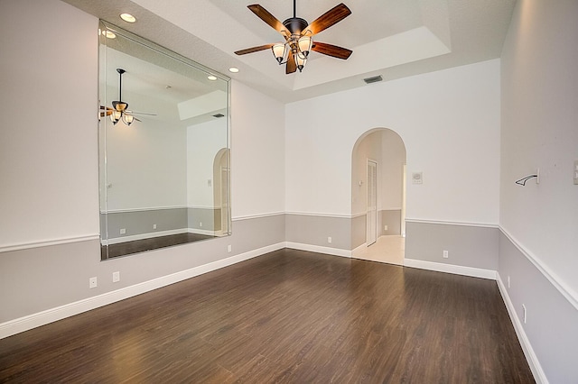 empty room with a raised ceiling, dark wood-type flooring, and ceiling fan