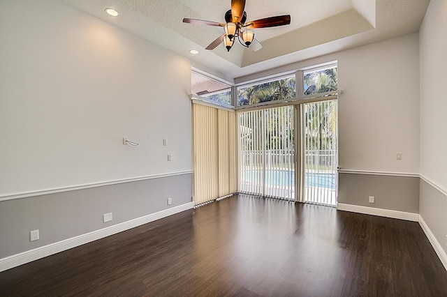 spare room featuring ceiling fan, dark wood-type flooring, a textured ceiling, and a raised ceiling