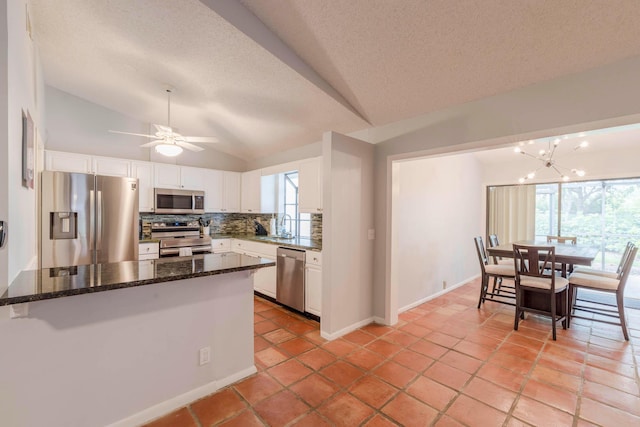 kitchen featuring stainless steel appliances, dark stone counters, white cabinetry, and lofted ceiling