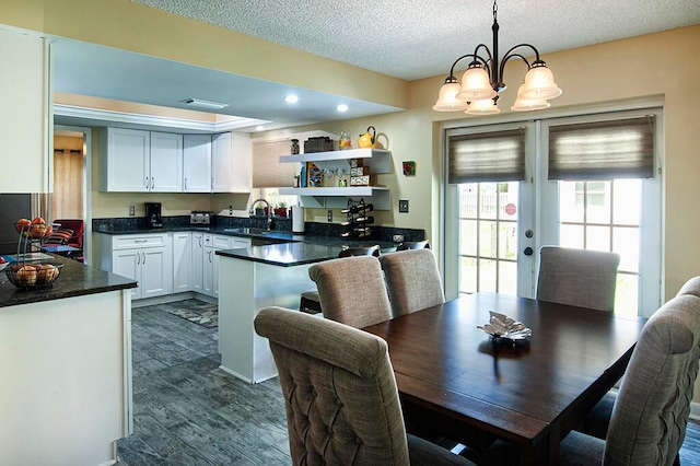 dining area with sink, dark wood-type flooring, a textured ceiling, and an inviting chandelier