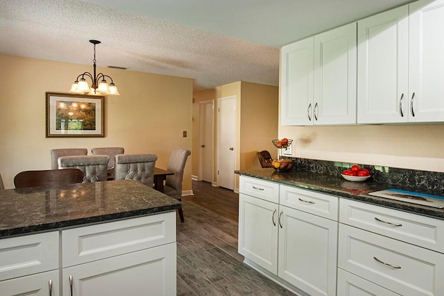 kitchen featuring dark hardwood / wood-style floors, white cabinets, dark stone countertops, decorative light fixtures, and a notable chandelier