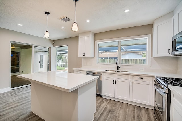 kitchen with decorative light fixtures, white cabinetry, sink, stainless steel appliances, and light wood-type flooring