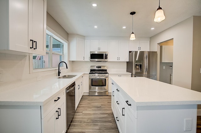 kitchen with hanging light fixtures, sink, light hardwood / wood-style flooring, stainless steel appliances, and white cabinets