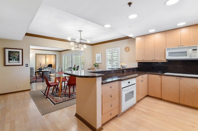 kitchen with light brown cabinetry, light hardwood / wood-style floors, white appliances, and kitchen peninsula