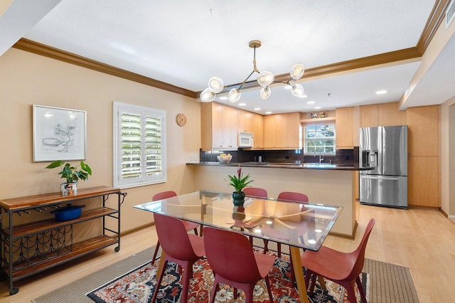 dining area with sink, crown molding, light wood-type flooring, and a chandelier