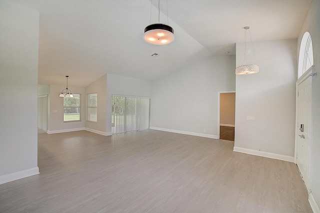 empty room with light hardwood / wood-style floors, a chandelier, and lofted ceiling