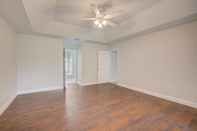 spare room featuring dark wood-type flooring, a raised ceiling, and ceiling fan