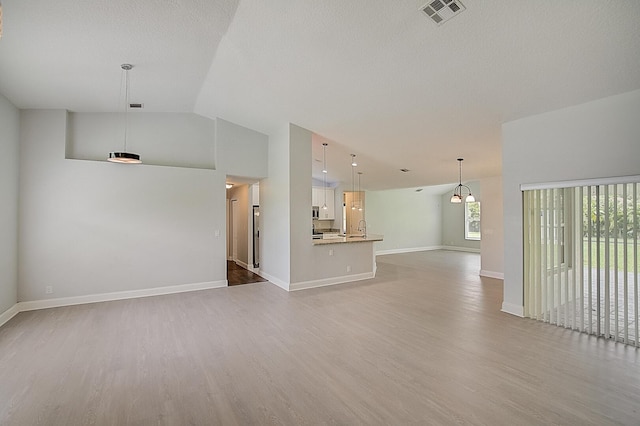 interior space with a textured ceiling, light hardwood / wood-style floors, and vaulted ceiling