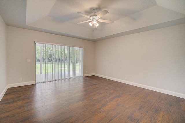 unfurnished room featuring a tray ceiling, dark wood-type flooring, ceiling fan, and a textured ceiling