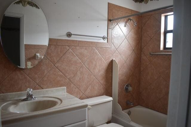 full bathroom with tiled shower / bath, toilet, vanity, and tile walls