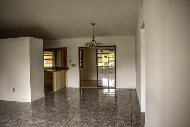 empty room with an inviting chandelier and dark tile flooring