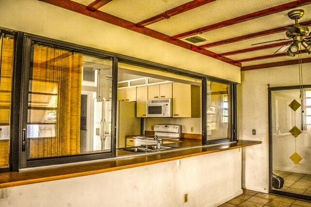 kitchen featuring beam ceiling, ceiling fan, stainless steel fridge with ice dispenser, dark tile floors, and range