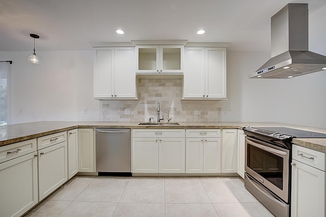 kitchen featuring kitchen peninsula, appliances with stainless steel finishes, wall chimney exhaust hood, hanging light fixtures, and sink