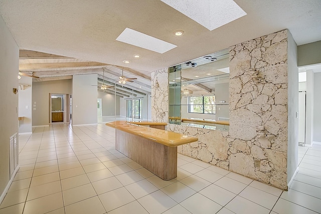 interior space with lofted ceiling with skylight, a textured ceiling, ceiling fan, and light tile flooring