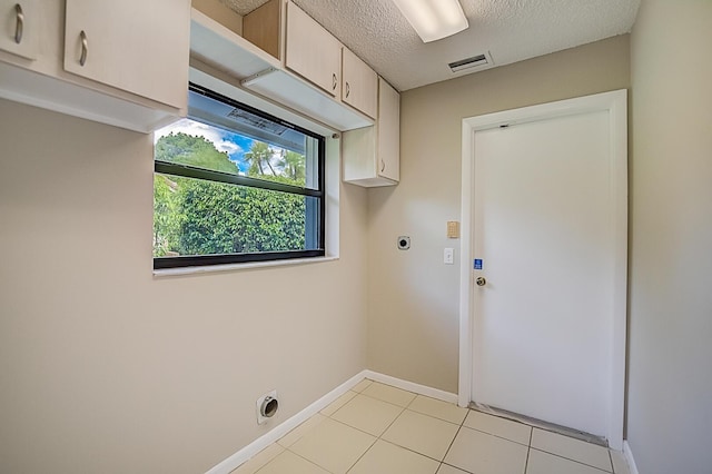 clothes washing area featuring electric dryer hookup, a textured ceiling, light tile flooring, and cabinets