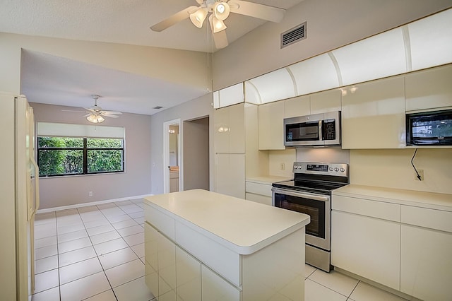 kitchen featuring ceiling fan, lofted ceiling, stainless steel appliances, light tile flooring, and a center island