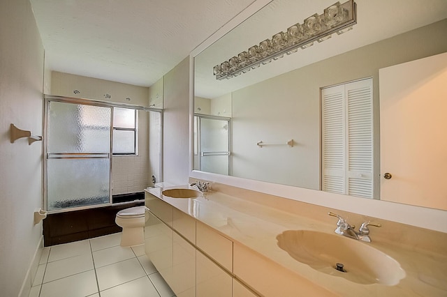 full bathroom with double sink vanity, toilet, tile flooring, and bath / shower combo with glass door