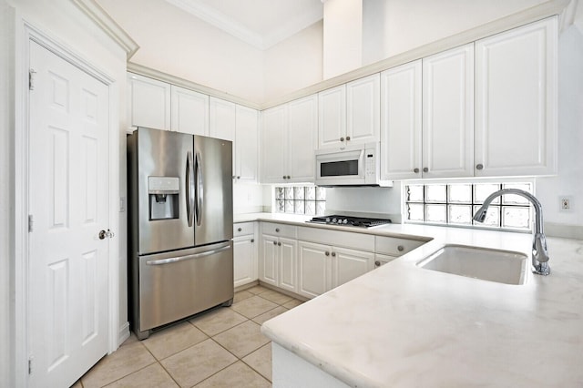 kitchen with sink, stainless steel appliances, light tile floors, white cabinets, and ornamental molding