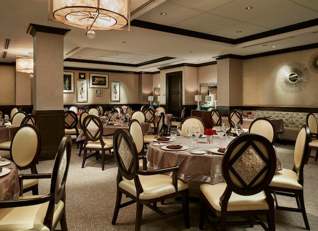 dining space with a raised ceiling, carpet floors, decorative columns, and ornamental molding