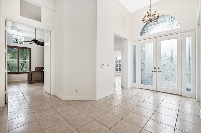 foyer entrance with light tile flooring, a high ceiling, french doors, and ceiling fan with notable chandelier